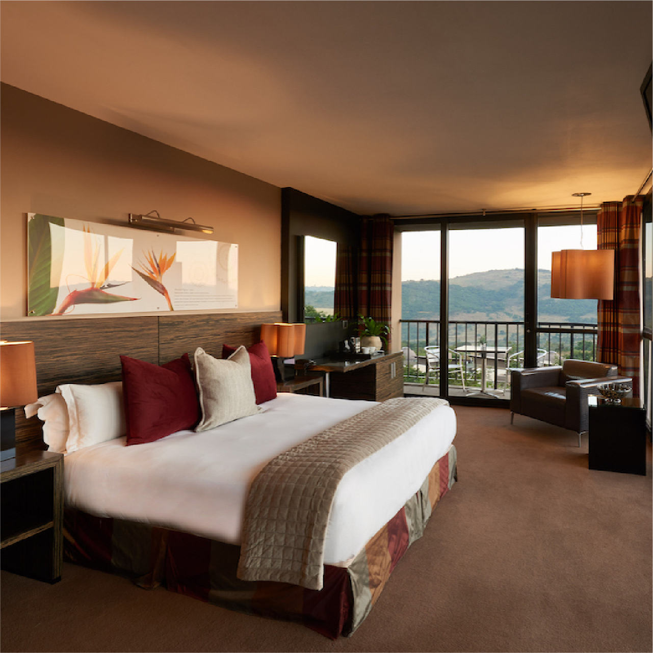 King Room - Garden View - Thaba Eco Hotel Elegant hotel room with a large bed, red and beige pillows, and warm lighting. A window reveals a mountain view, creating a cozy, inviting atmosphere.